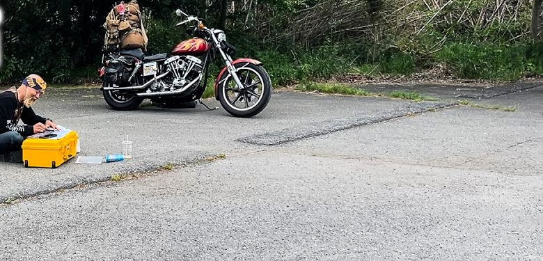 路肩のアスファルト。奥に荷を積んだバイクと、路面に座る人物が小さく写る