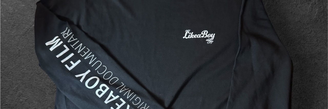 アスファルトの上に平置きされた黒いロンT。袖に LIKEABOY FILM ORIGINAL DOCUMENTARY の罫囲みが入っている